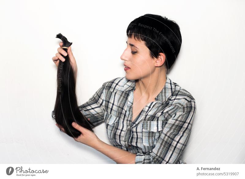 Eine junge Frau mit kurzen Haaren zeigt eine Haarpartie in einem Pferdeschwanz, die sie gerade geschnitten hat. Konzept der Haarspende für Krebspatienten