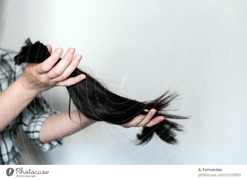 Junge Frau hält eine Haarpartie in einem Pferdeschwanz, die sie gerade abgeschnitten hat. Konzept der Haarspende für Krebspatienten Haarschnitt Überarbeitung