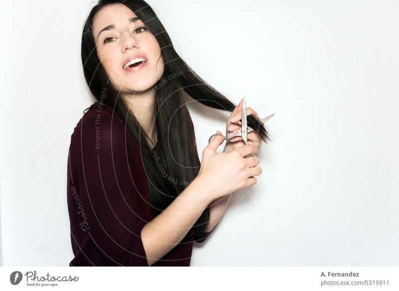 Schöne fröhliche junge Frau, die mit einer Schere die Enden ihres langen schwarzen Haares abschneidet Haarschnitt Behaarung Abschnitt Haarpartie Beteiligung