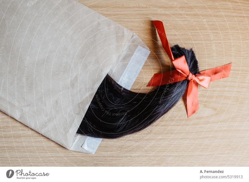 Abgeschnittenes Haar in einem Pferdeschwanz in einem Umschlag. Konzept der Haarspende für Krebspatienten per Post Haarschnitt schenken Geldgeschenk Behaarung