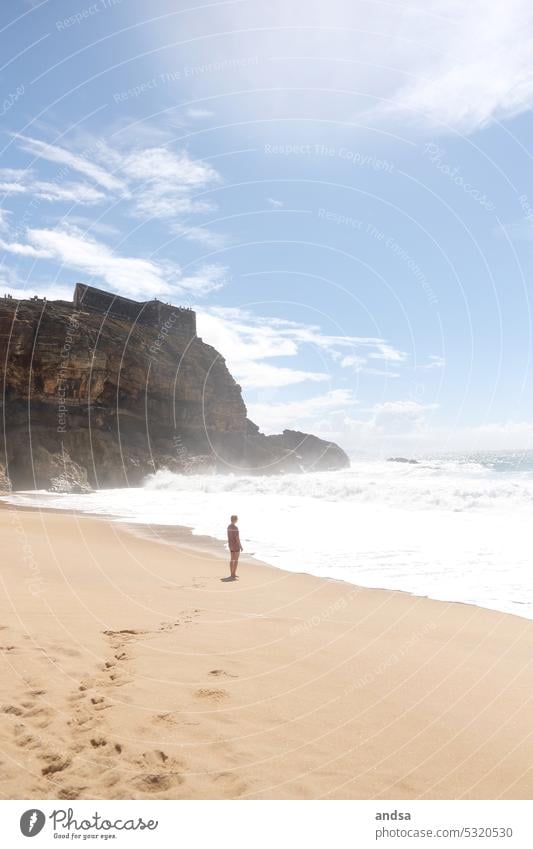 Frau am Strand schaut aufs Meer hinaus Kliff Wellen Sand Sandstrand Portugal Nazare Küste Schönes Wetter Wasser Außenaufnahme Natur Sommer