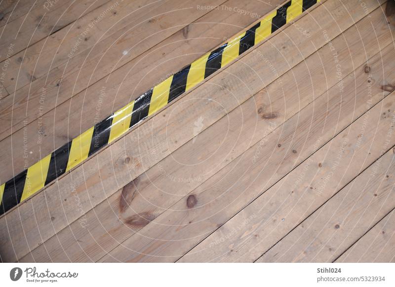 schwarz-gelbes Klebeband auf Holzdielenboden gelb-schwarz gestreift Warnung gefahr Stolpern Stolperfalle Holzfußboden Dielenboden Altbau Farbfoto Warnhinweis