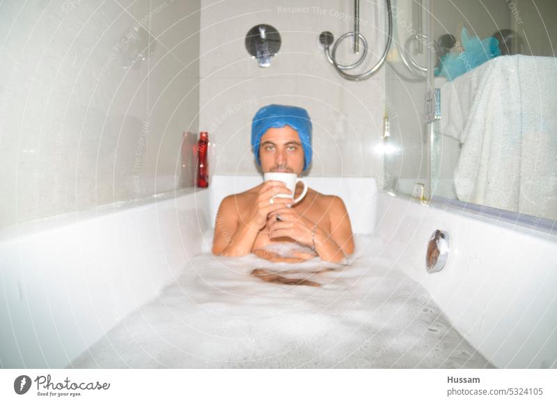 Foto von einem Mann in der Badewanne, der sich entspannt und eine Tasse Tee trinkt und eine Plastiktüte auf dem Kopf trägt ein Bad nehmen Freizeit Spaß Reichtum