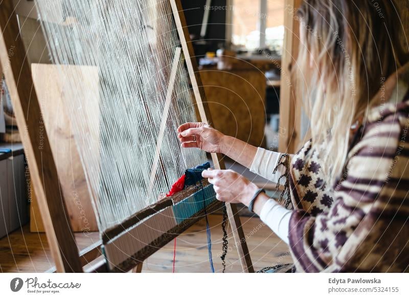 Handwerkliche Frau beim Weben am Webstuhl in ihrer Werkstatt echte Menschen Strickmaschine Wolle Garn Weberei Kompetenz Kleidungsstück Herstellung Material