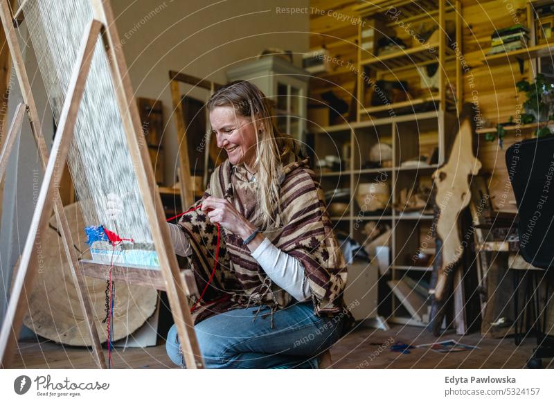 Handwerkliche Frau beim Weben am Webstuhl in ihrer Werkstatt echte Menschen Strickmaschine Wolle Garn Weberei Kompetenz Kleidungsstück Herstellung Material