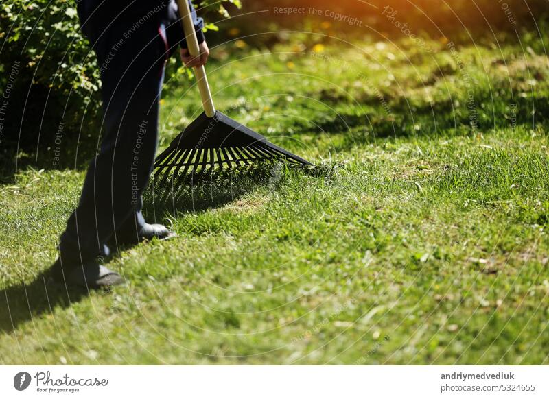 Unbekannter Mann harkt Blätter mit einer schwarzen Plastikharke zusammen. Reinigung von Müll und trockenem Gras aus dem Rasen mit einem Fächerbesen. Konzept der Vorbereitung des Gartens für den Winter, Frühling. Pflege des Gartens