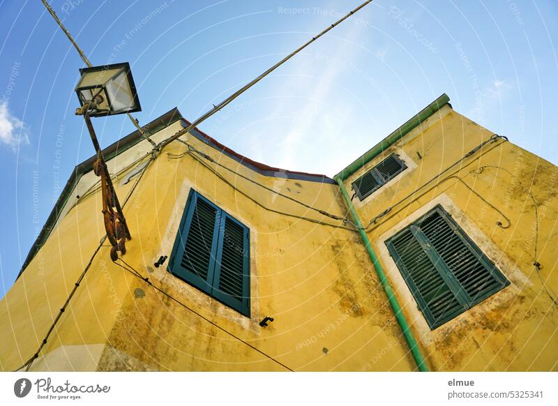 wohnen auf Elba - verwinkeltes gelbes Wohngebäude mit Fensterläden vor den Fenstern und einer Straßenlampe aus der Froschperspektive Wohnhaus Poggio Italien