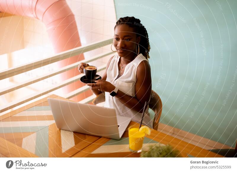 Junge schwarze Frau trinkt Kaffee und arbeitet am Laptop im Café Afrikanisch Afroamerikaner Afro-Look Afrofrisur attraktiv charmant Mitteilung Computer Tag