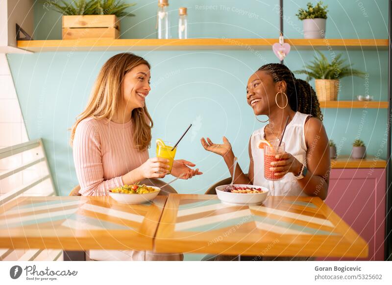 Junge schwarze und kaukasische Frau, die sich amüsiert, frische Säfte trinkt und im Café gesund frühstückt Afrikanisch afrikanische Frau attraktiv schön