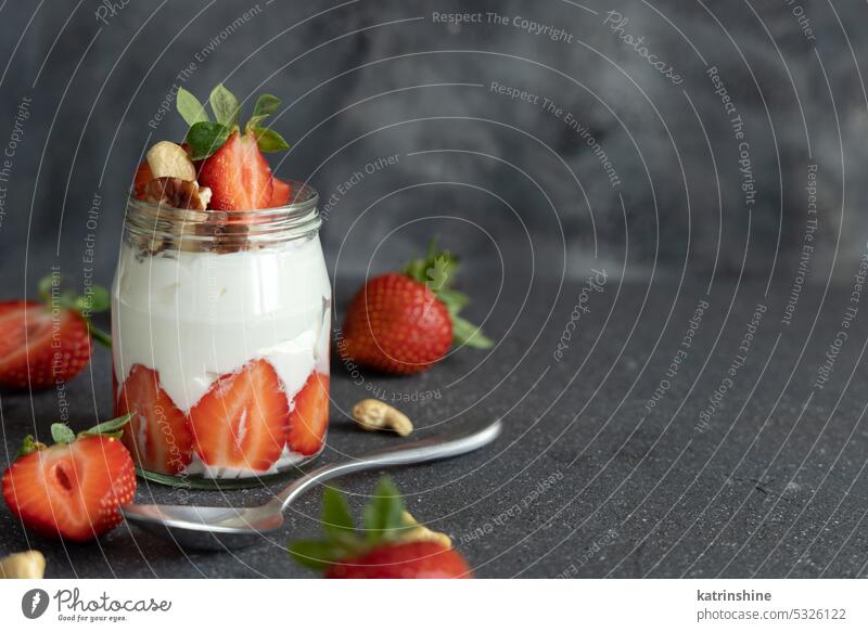 Griechischer Joghurt, Nüsse und Erdbeeren in einem Glasgefäß auf einem grauen Tisch mit einem Löffel, Nahaufnahme, Kopiervorlage Muttern erdbeeren Frühstück