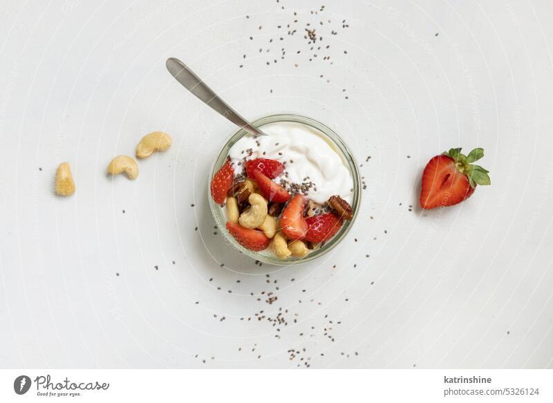 Griechischer Joghurt, Nüsse und Erdbeeren in einem Glasgefäß mit einem Löffel auf einer weißen Tischplatte Muttern erdbeeren Frühstück Draufsicht Textfreiraum
