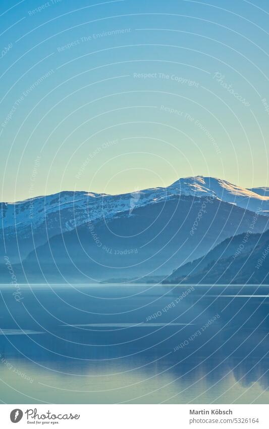 Blick auf den See Oppstrynsvatnet in Norwegen in den Morgenstunden. Schneebedeckte Berge Gebirgssee Skandinavien Sonnenschein Frühnebel Reflexion & Spiegelung