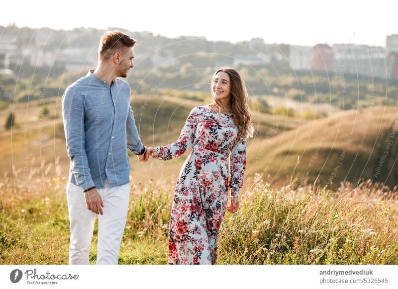 Junges Paar umarmt und geht im Sommer Feld mit Gras auf dem Hintergrund der Stadt. Mann und Frau. Konzept der schönen Familie. jung Sonne romantisch
