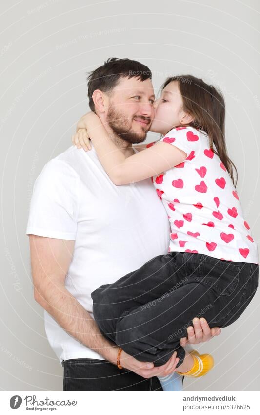 junger Vater hält seine kleine Tochter in seinen Händen. Vater umarmt sein Kind mit Liebe und Kind küssen ihn. Mann in weißem T-Shirt und Mädchen in T-Shirt mit roten Herzen. Alles Gute zum Vatertag. valentine's day