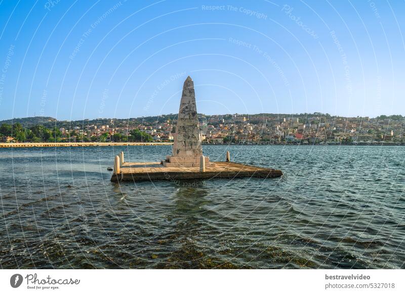 1813 aus Stein gebauter, von Wasser umgebener Obelisk neben der De-Bosset-Brücke mit dem Stadtpanorama von Argostoli im Hintergrund auf der Ionischen Insel Kefalonia Griechenland.