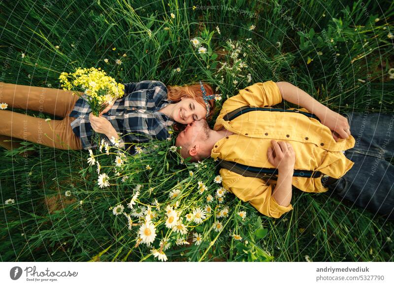 glückliches junges Paar, Mann und rothaarige Frau, liegen auf hellgrünem Gras an einem Sommertag, Ansicht von oben. Liebesgeschichte. Zusammensein Mädchen