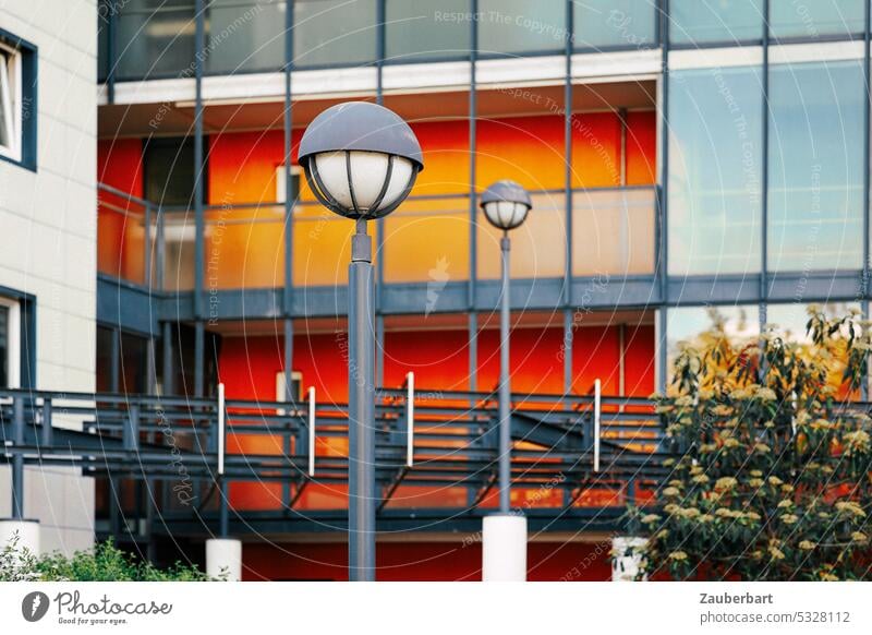 Straßenlaternen vor rot-grauer, rechteckig gegliederter Fassade straßenbeleuchtung 70er 60er modern architektur urban öde banal farbig Buschwerk duo zwei
