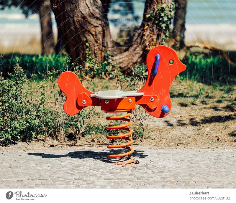 Federwippe, rotes Holztier zum Reiten für Kinder auf Stahlfeder, dahinter Baum und Strand Spiel wippen Bewegung Spielzeug Spielplatz Spirale reiten Stand Spaß
