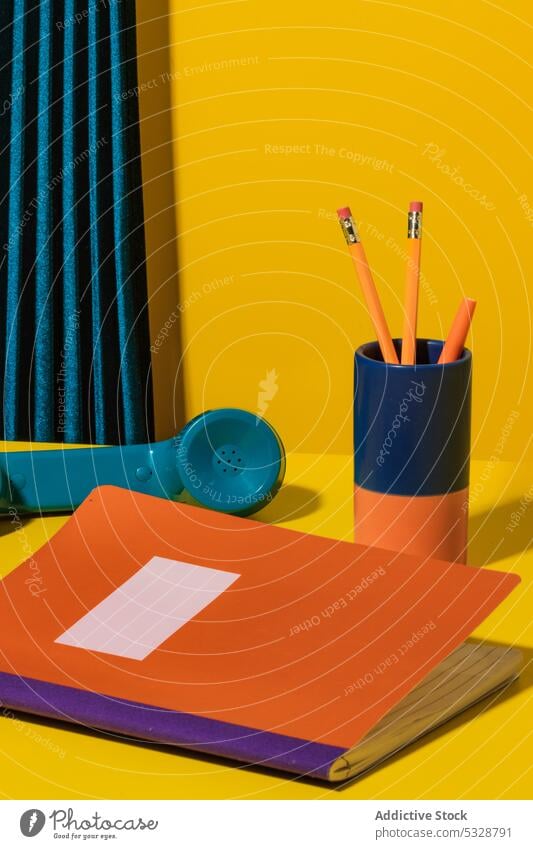 Buntes Schulmaterial auf dem Schreibtisch neben dem Telefon Schule Vorrat Schönschreibheft Mobilteil ruhend Arbeitsbereich farbenfroh mehrfarbig altmodisch hell
