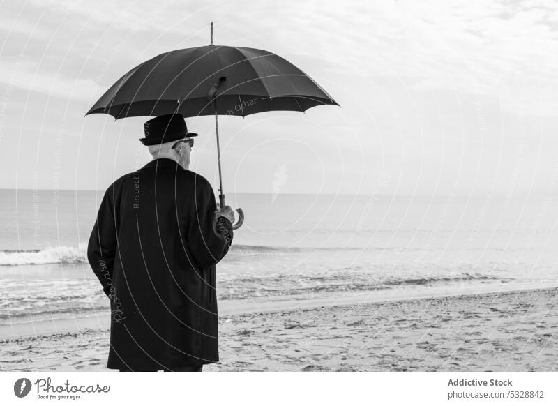 Unerkennbar reifer Mann in gemütlichem Anzug mit Sonnenschirm am Sandstrand Strand MEER Regenschirm Ufer einsam Einsamkeit Meer winken Melancholie Küste