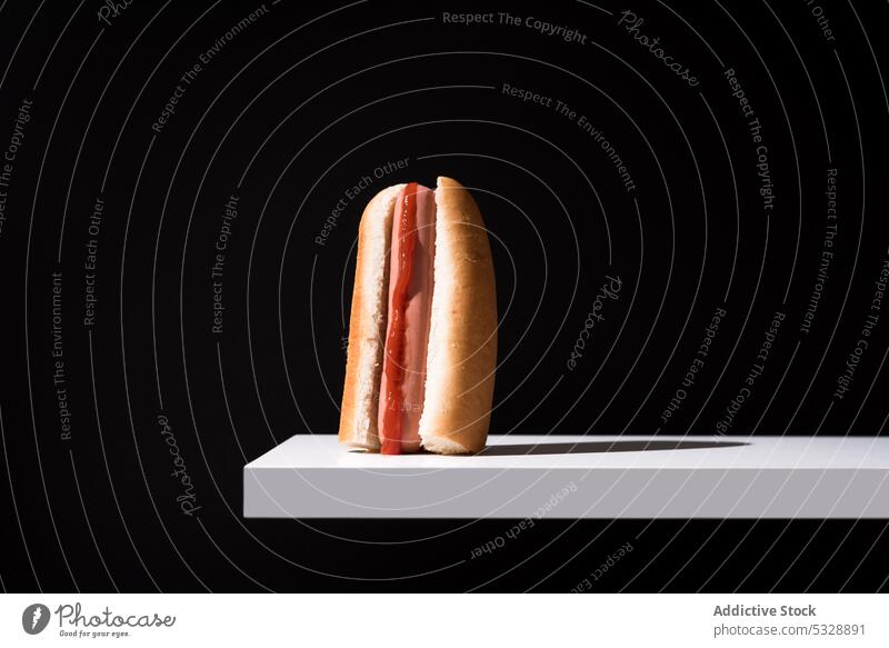 Leckerer Hot Dog auf weißem Brett vor schwarzem Hintergrund Brötchen Hotdog lecker Holzplatte Fastfood Snack frisch Lebensmittel süß Mahlzeit Ernährung