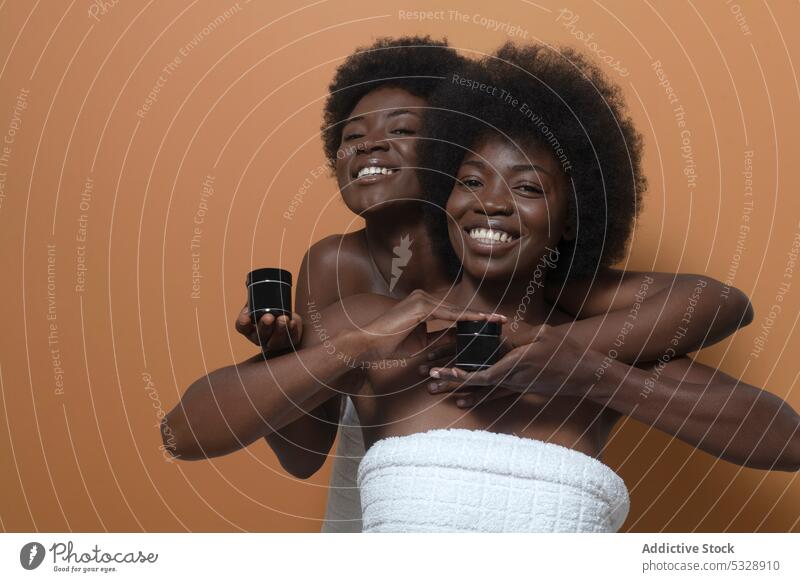 Fröhliche schwarze Frauen zeigen Flaschen mit Kosmetika Model Hautpflege Sahne Attrappe inserieren Lächeln Afro-Look heiter Glück krause Haare positiv