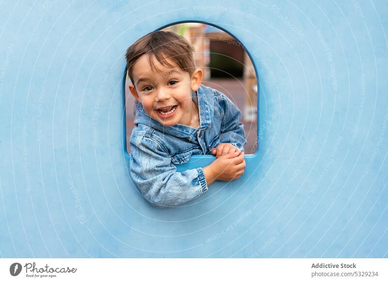 Glückliches kleines Kind, das aus der blauen Wand herausschaut Junge spielen schauen Sie Spielplatz heiter Freude Lächeln spielerisch Fenster Kindheit Spaß