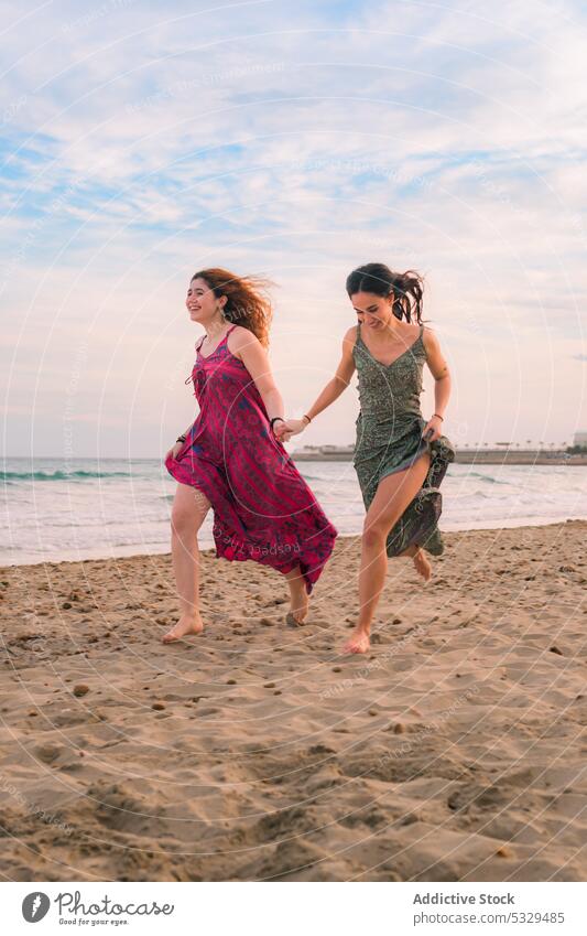 Glückliche Frauen laufen am Sandstrand Freund Händchenhalten heiter MEER Freundschaft Seeküste Strand Barfuß Sommer Zusammensein sorgenfrei Urlaub Kleid Lächeln