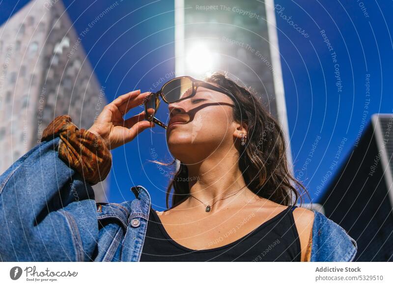 Stilvolle Frau mit Sonnenbrille auf der Straße an einem sonnigen Tag Großstadt Wolkenkratzer Revier urban Megapolis Jacke Abheben Augen geschlossen modern
