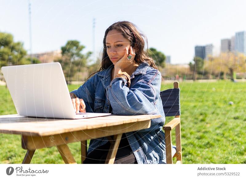 Frau arbeitet an einem Laptop im Park freiberuflich Arbeit Browsen benutzend Telearbeit Internet jung Gerät Netbook Apparatur hölzern selbständig Sonne Beruf
