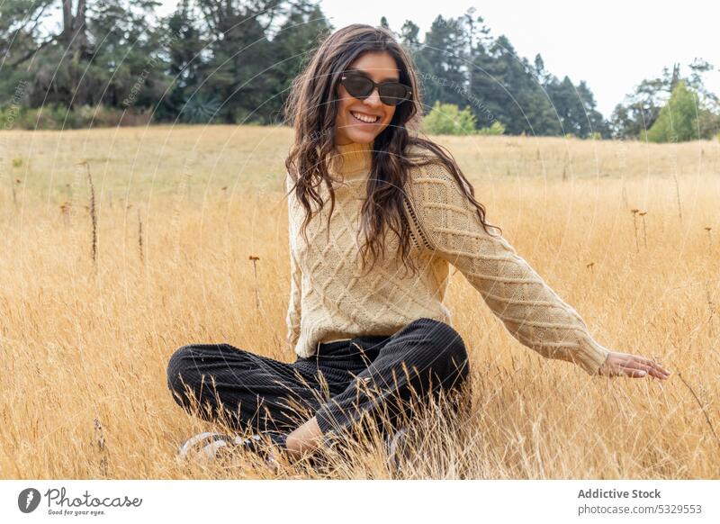 Lächelnde Frau mit Sonnenbrille, die sich auf einem Feld mit trockenem Gras ausruht Wiese Natur Landschaft Wellenhand Sonnenlicht sich[Akk] entspannen heiter