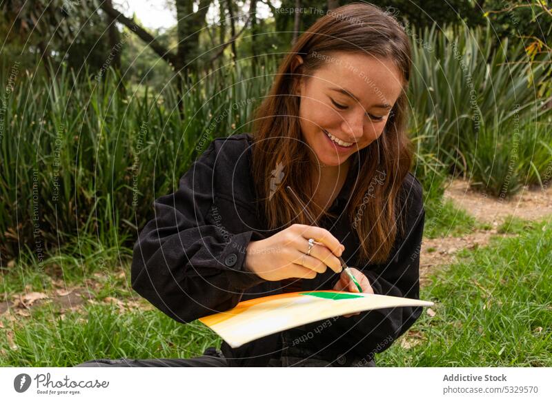 Fröhliche junge Frau beim Zeichnen in der Natur Farbe Künstler Anstreicher heiter ruhen Glück Lächeln Hobby zeichnen Inspiration Pinselblume kreativ Kunst