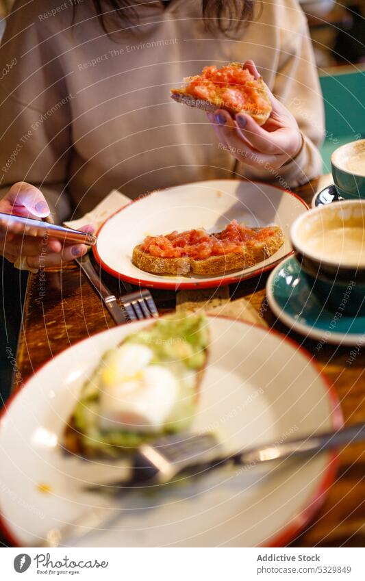 Unbekannte Frau isst leckere Tomatentoasts essen Frühstück Smartphone Café Zuprosten Kaffee benutzend Cappuccino Tisch Browsen Mahlzeit Morgen Lebensmittel