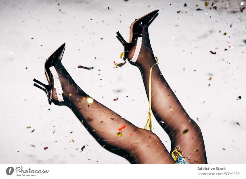 Crop Frau in stilvolle Schuhe mit Konfetti während der Party angehobene Beine Strumpfhose feiern festlich Stil Damenschuhe Feiertag eng farbig Papier Nylon