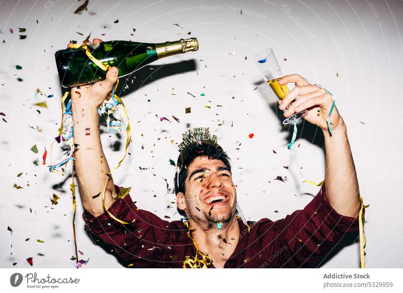 Fröhlicher Mann mit Champagner zum Neujahrsfest Glück Alkohol trinken feiern Arme hochgezogen Party Porträt festlich Flasche Konfetti alkoholisch dekorativ
