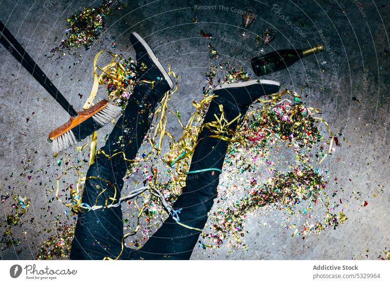 Crop betrunkener Mann mit Konfetti auf dem Boden während einer Party feiern Schnaps festlich Feiertag Champagne müde unordentlich Besen Stock Lügen farbig