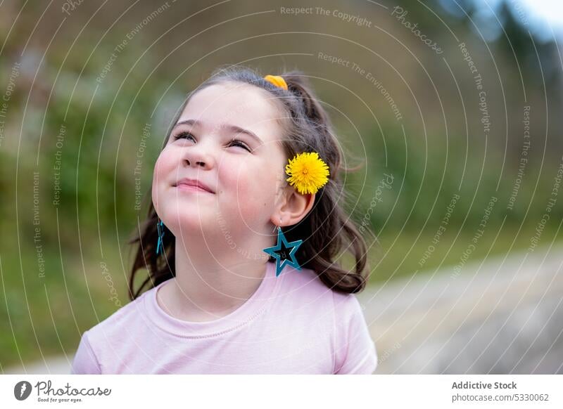 Glückliches stehendes Mädchen mit gelben Blumen im Haar Kind Ohr Behaarung Ohrringe Park Lächeln Natur Sommer niedlich heiter wenig hell positiv Freude
