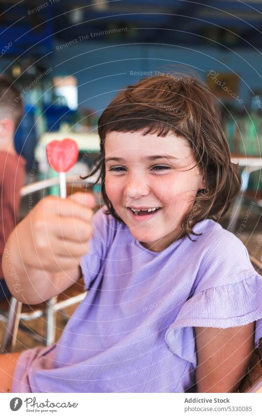 Lächelndes Mädchen mit leckerem Lutscher im Café Lollipop Kind süß Kleid Dessert positiv Vorschule heiter Glück Kindheit bezaubernd niedlich Bonbon Freude