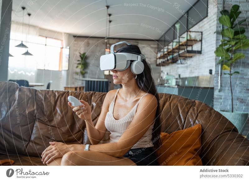 Frau in VR-Headset interagiert mit digitaler Welt mithilfe von Controllern Videospiel interagieren spielen Regler Virtuelle Realität Sofa heimwärts Erfahrung
