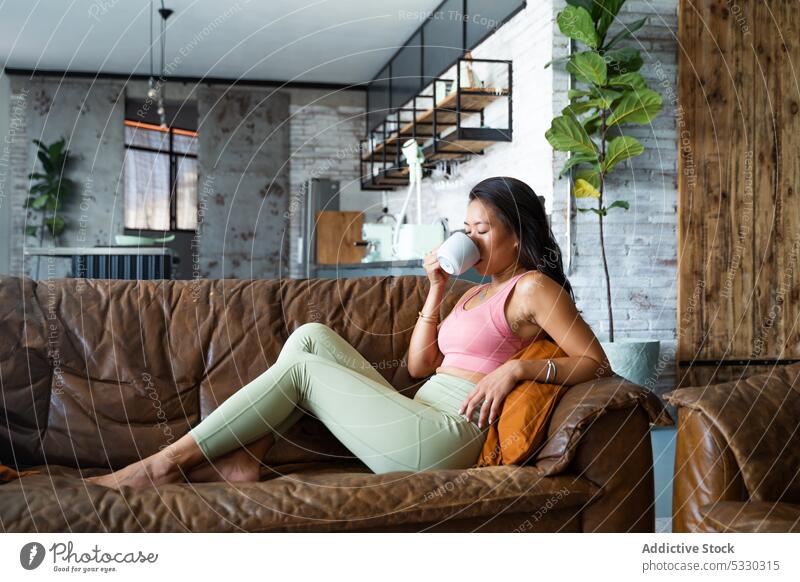Entspannte Frau trinkt Kaffee auf Sofa in gemütlichem Zimmer trinken ruhen Heißgetränk heimwärts Komfort sich[Akk] entspannen Wohnzimmer lässig jung Tasse