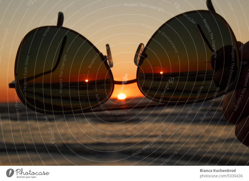Sonnenbrille die auf den Sonnenuntergang am Meer zeigt was wie ein Gesicht aussieht. Wasser Sonnenlicht Sonnenstrahlen Außenaufnahme Landschaft Objekt Natur