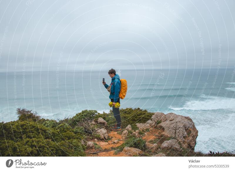 Ein Abenteurer, der auf dem Fisherman Trail in der portugiesischen Algarve-Region wandert, fotografiert das Meer, das bei dem regnerischen Wetter zum Leben erwacht ist. Die Kraft des Wassers
