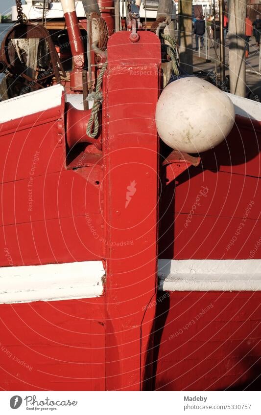 Bug eines alten roten Fischkutter mit weißem Streifen bei Sonnenschein im Hafen von Neuharlingersiel an der Küste der Nordsee bei Esens in Ostfriesland in Niedersachsen