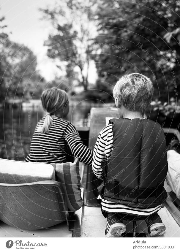 Rückenansicht zweier Kinder auf einem Tretboot auf einem See Kindheit Wasser Ausflug sitzen hocken Streifen Ufer steuern treten Schwimmweste Bäume