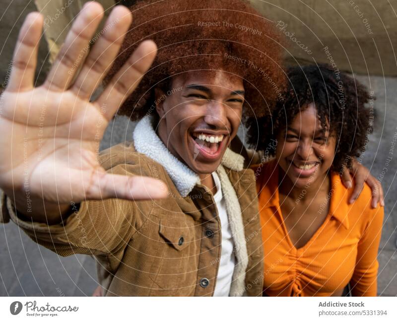 Lächelndes schwarzes Paar steht in Umarmung und lacht in die Kamera Hallo Hi heiter Gruß gestikulieren Glück Porträt freundlich Afroamerikaner ethnisch positiv