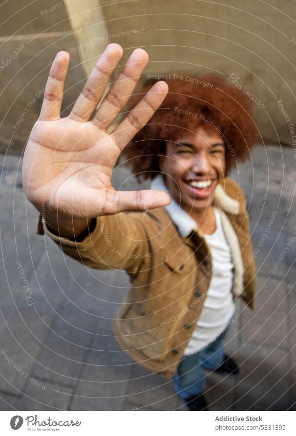 Fröhlicher schwarzer Mann, der auf der Straße eine Geste zur Begrüßung zeigt gestikulieren heiter Symbol Lächeln Zeichen Vorschein Glück Großstadt urban