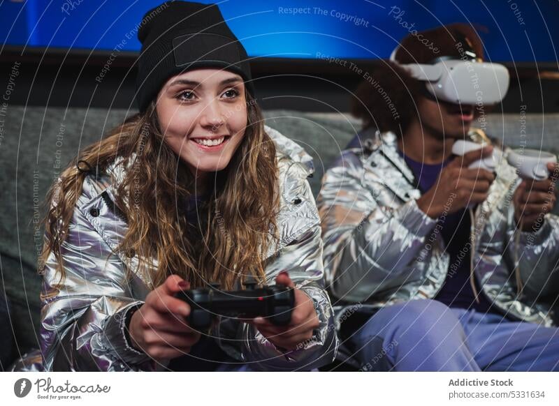 Männliche und weibliche Videospieler in futuristischer Kleidung auf einer Couch Spieler spielen unterhalten Vergnügen Regler Konsole Gamepad Mann Frau Freund