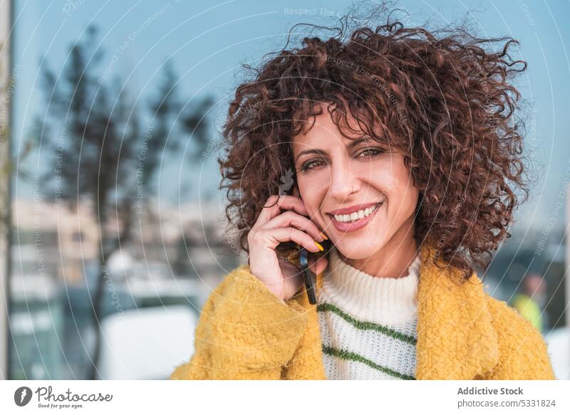 Vergnügte Frau, die auf der Straße mit einem Mobiltelefon spricht Smartphone reden Anruf Lächeln Telefonanruf positiv sprechen Kommunizieren lässig Apparatur