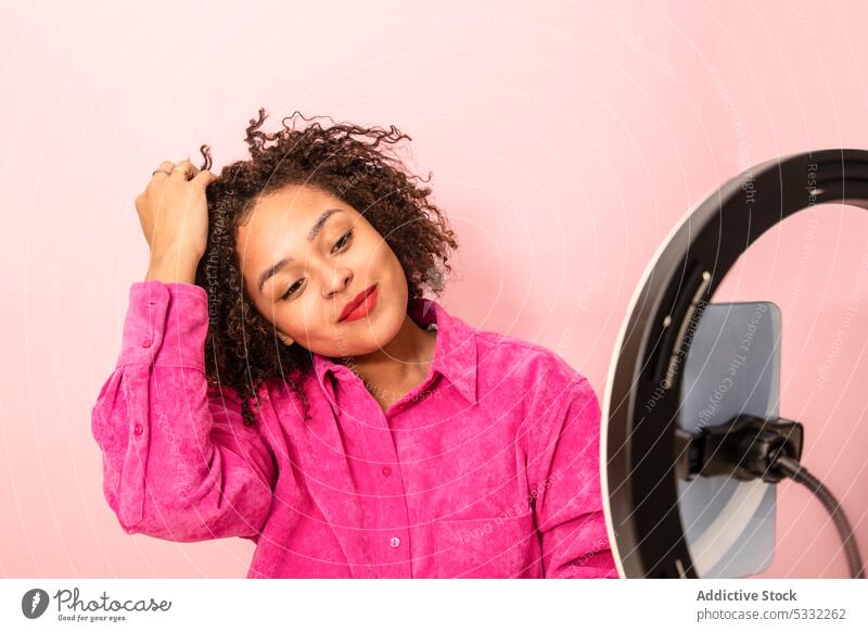 Ruhige ethnische Frau, die während eines Schönheitstutorials eine Frisur vorführt Blogger vlog Ringlampe Smartphone manifestieren Influencer Aufzeichnen teilen