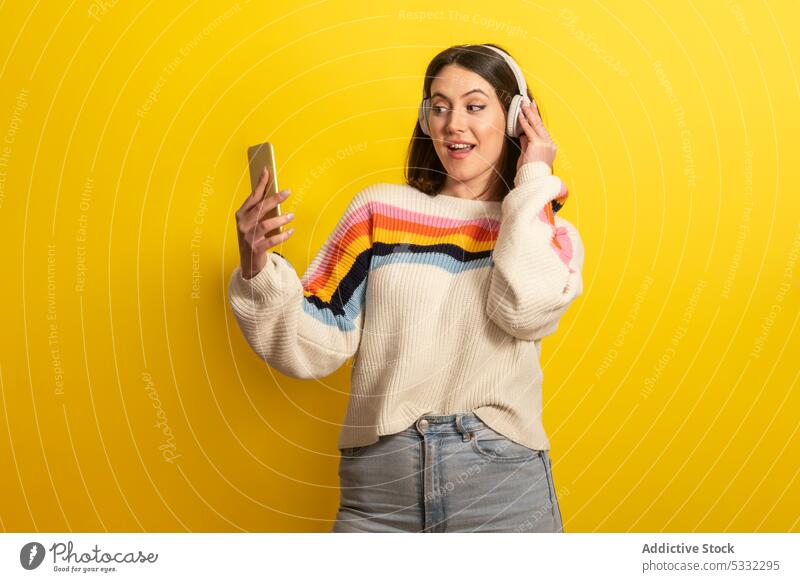 Lächelnde Frau mit Smartphone hört Musik auf gelbem Hintergrund zuhören Kopfhörer Glück Gerät heiter positiv modern Drahtlos jung hell lässig Gesang lebhaft